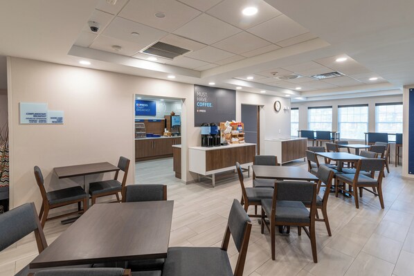 A modern dining area with tables and chairs, a coffee station, and a clock on the wall.