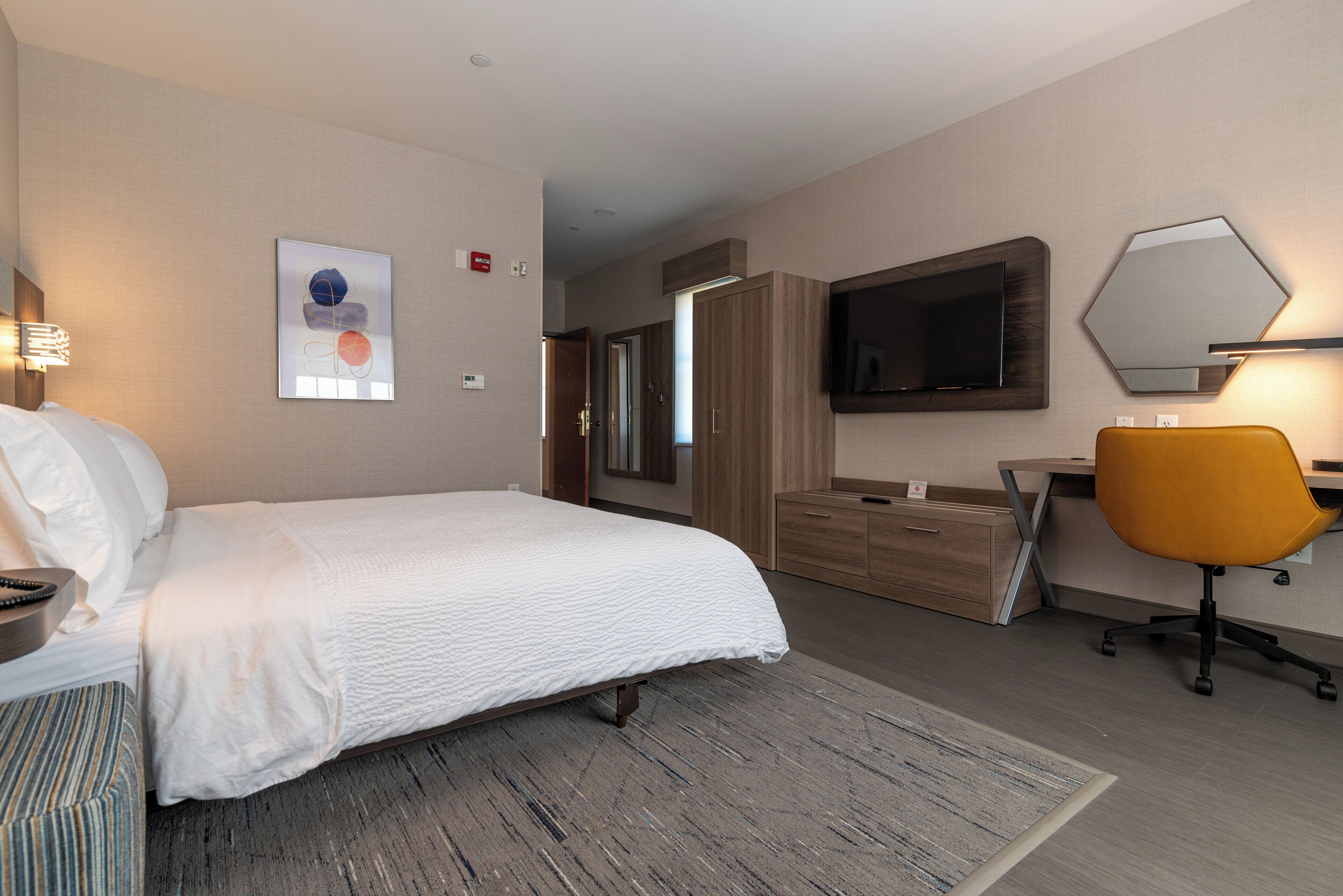 A hotel room with a bed, a desk, a chair, a television, and a large mirror.