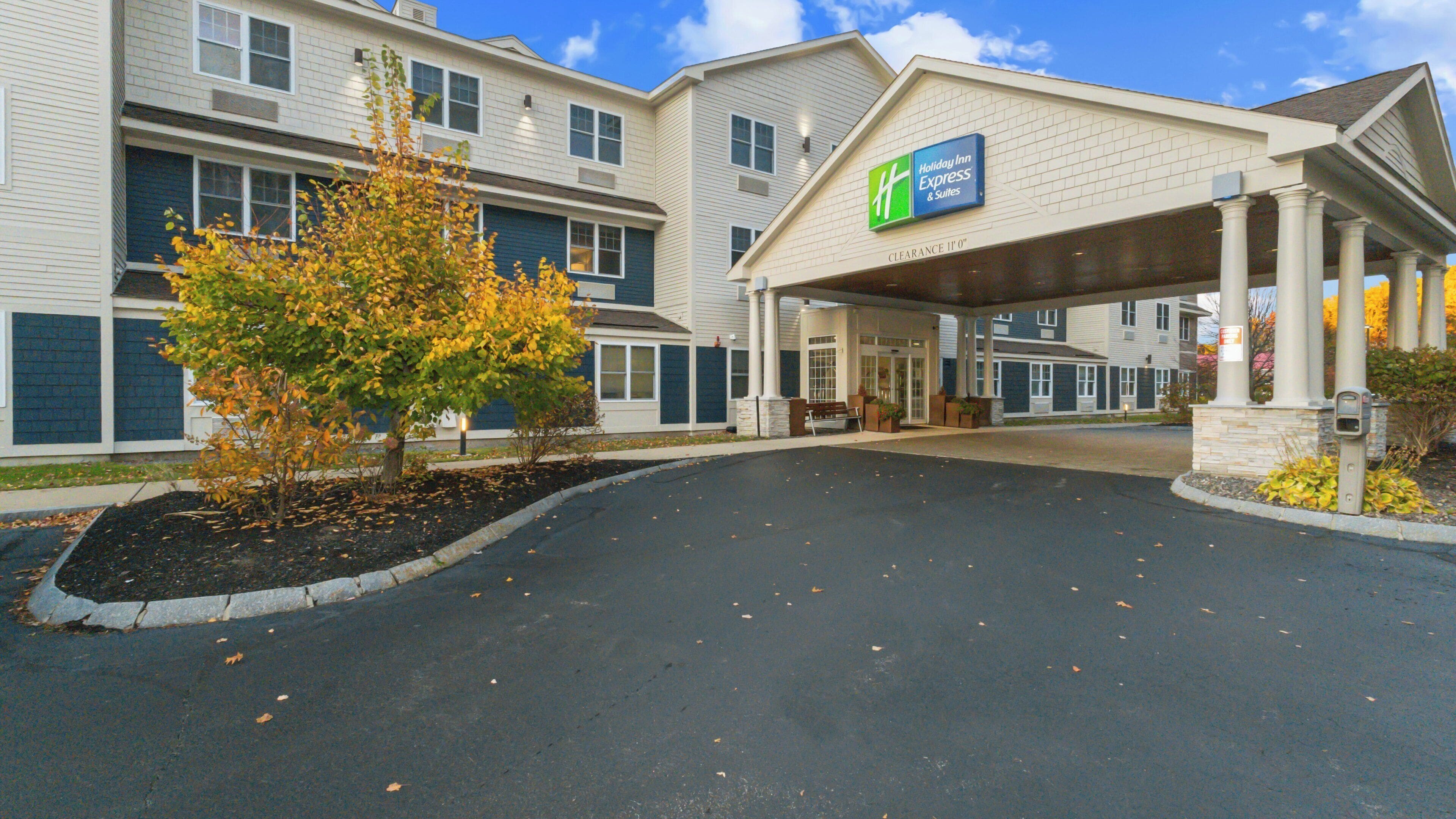 A Holiday Inn Express & Suites with a covered entrance, a landscaped driveway, and a tree with autumn leaves.
