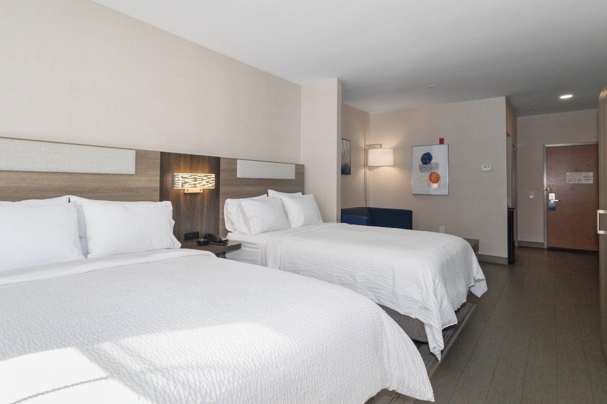 A hotel room with two beds, a nightstand, a lamp, and a door.