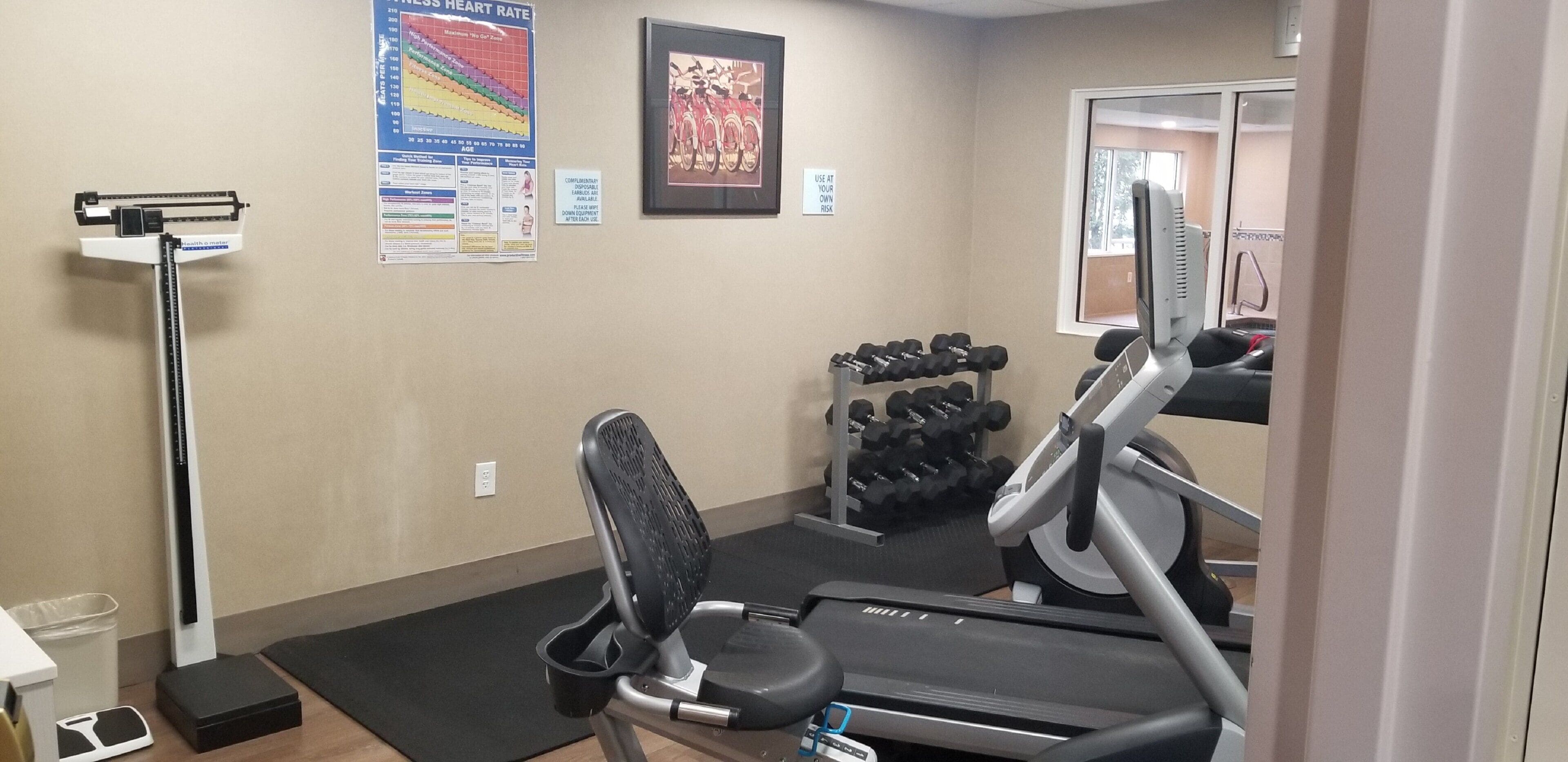 Un gimnasio con equipamiento de ejercicio, una cinta de correr y un soporte de mancuernas en la pared.