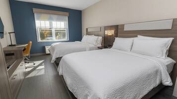 A hotel room with two beds, a desk, a chair, and a window.