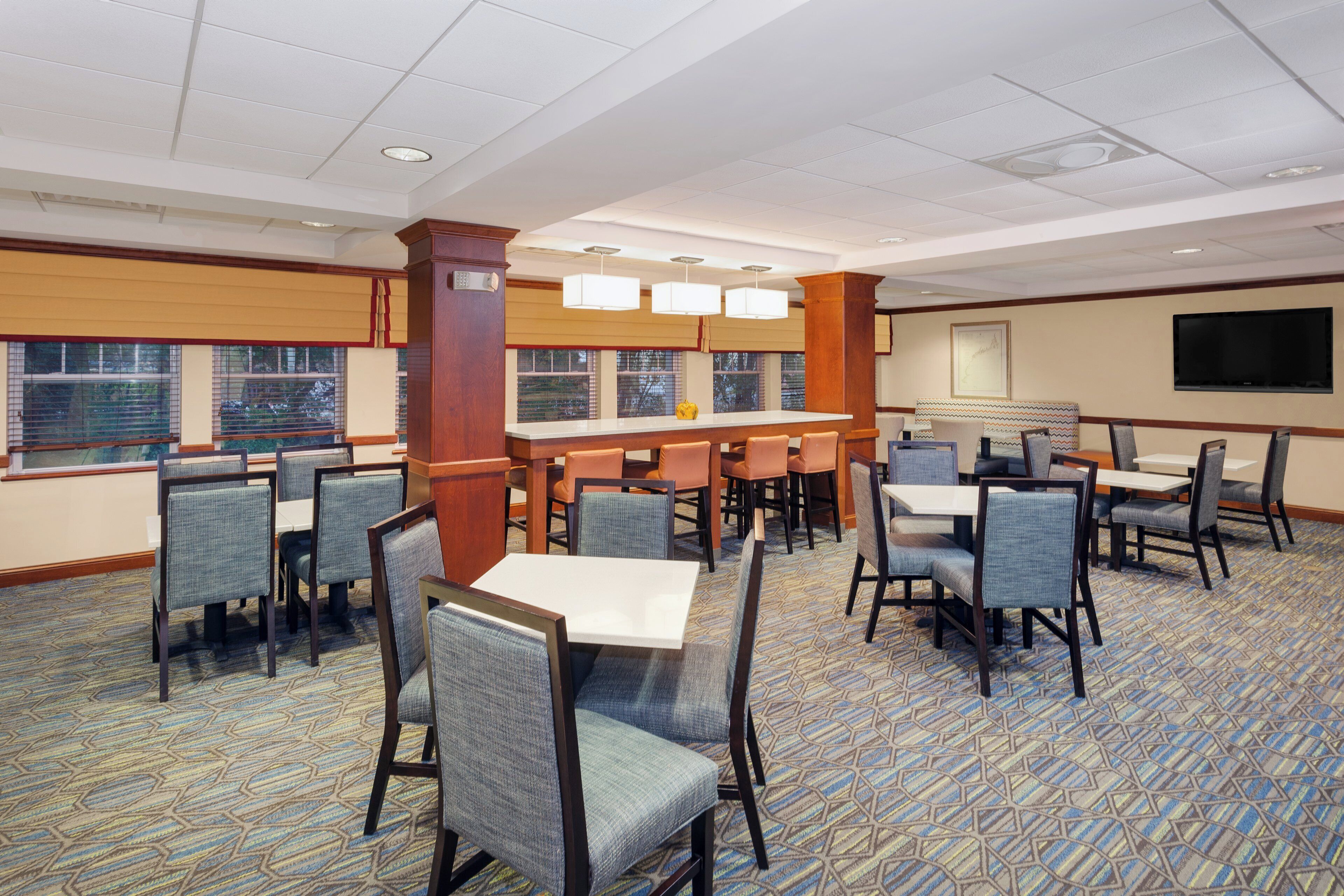 A hotel dining area with multiple tables and chairs, a bar, and large windows.