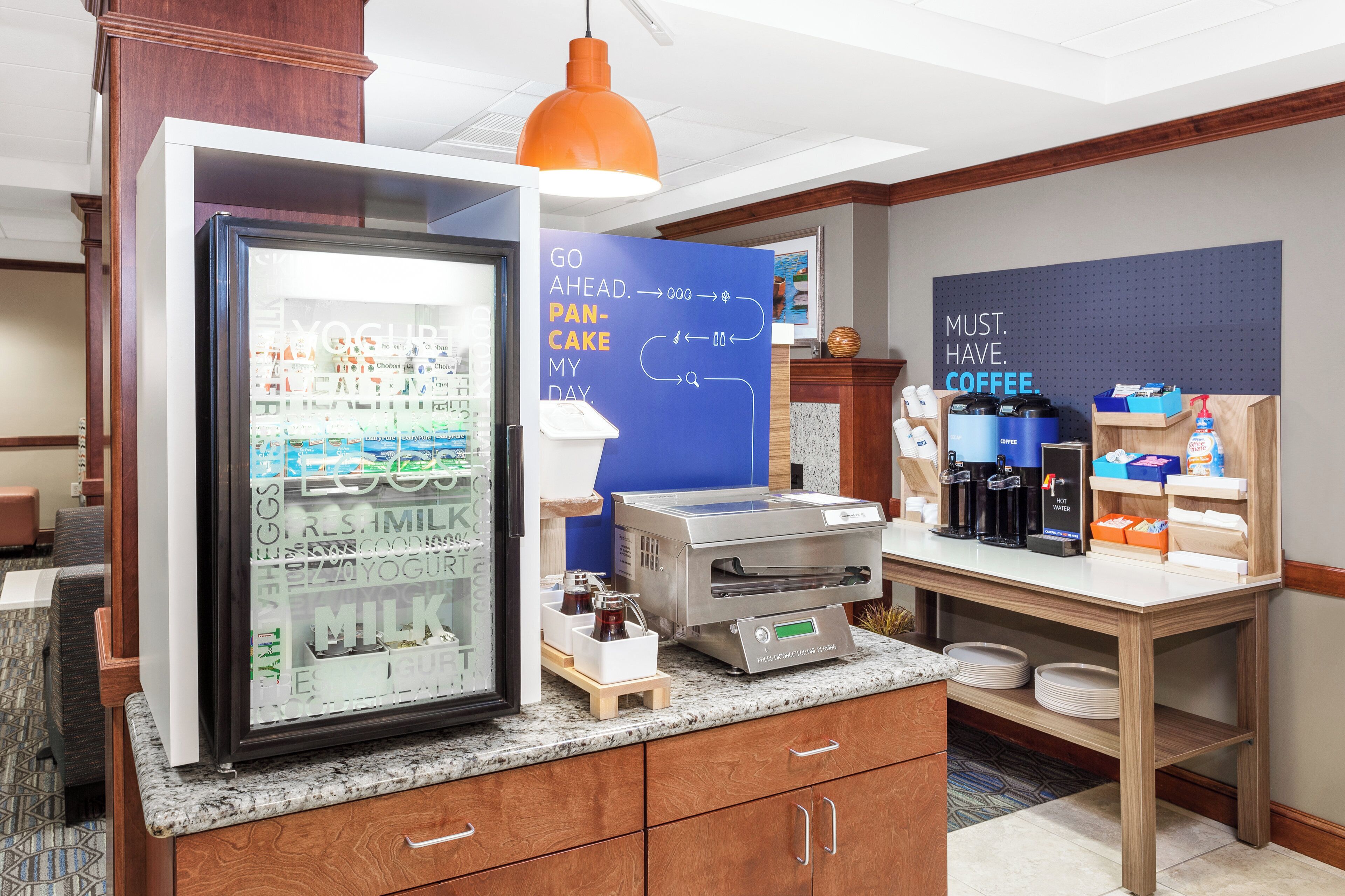A breakfast bar with a refrigerator stocked with dairy products, a coffee station, and a wall with motivational quotes.
