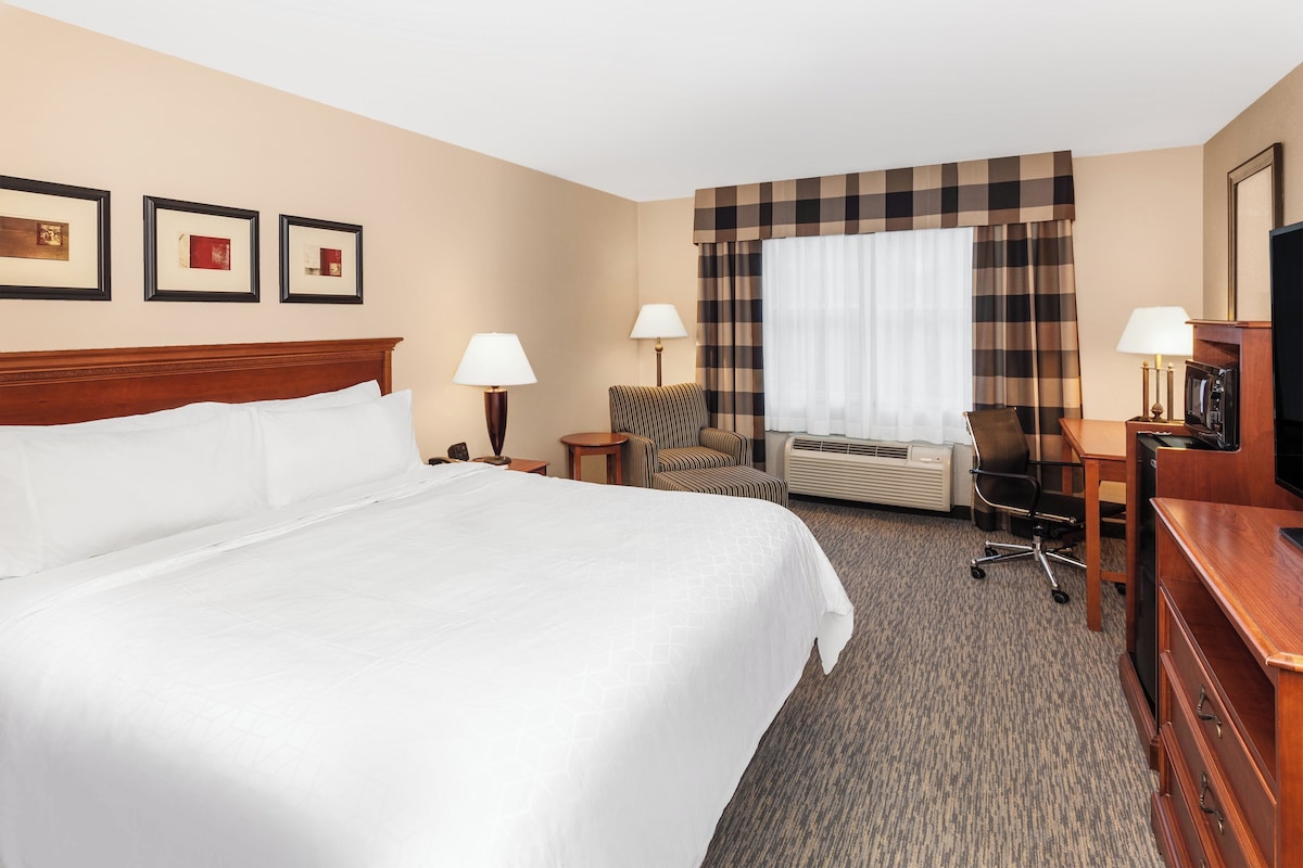 A hotel room with a large bed, two bedside tables, a desk, a chair, an air conditioning unit, and a television.