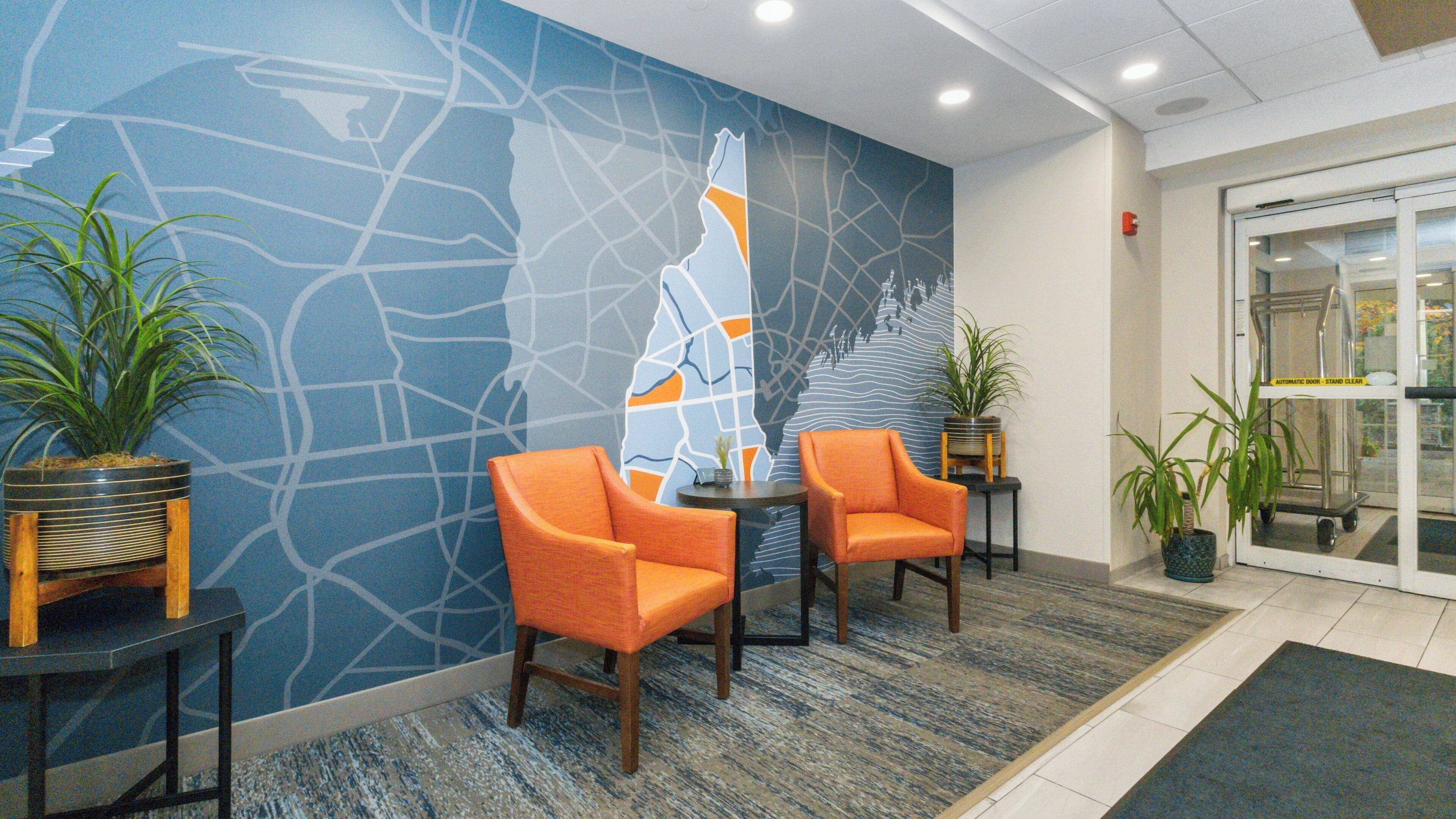 Un vestíbulo con un mural de un mapa, dos sillones naranja y plantas en macetas.