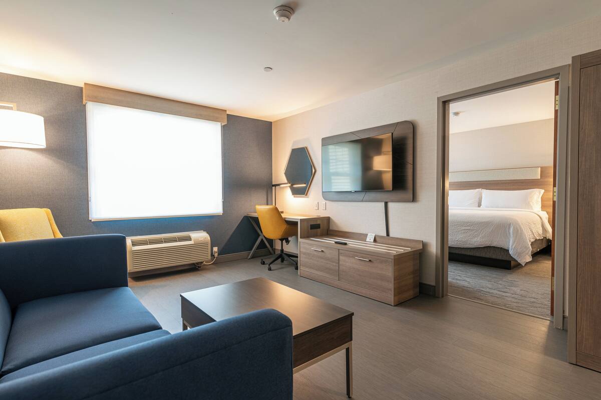 A modern hotel room with a sofa, desk, chair, TV, and a bed.
