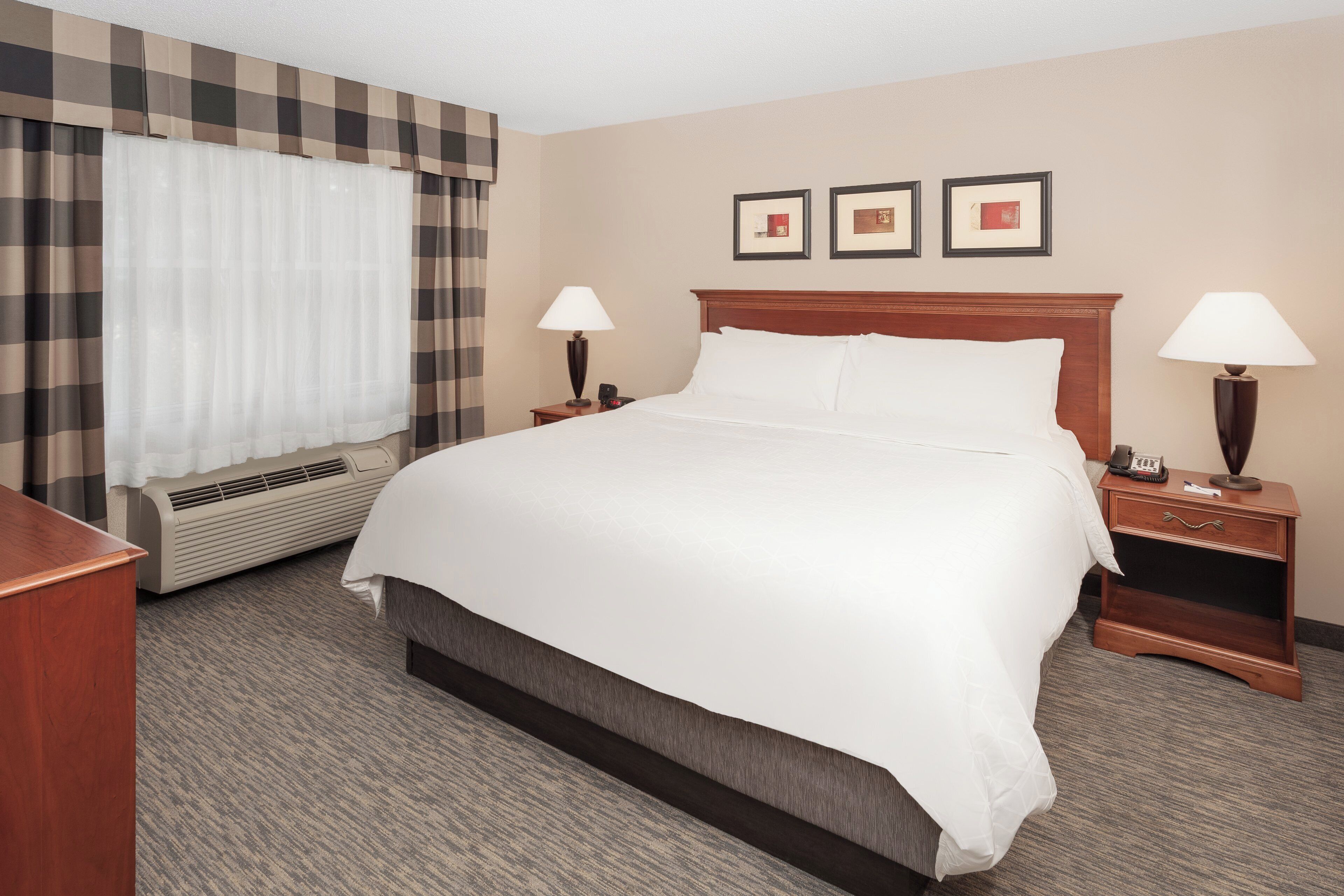 A hotel room with a large bed, two bedside tables with lamps, a heater, and a window with curtains.