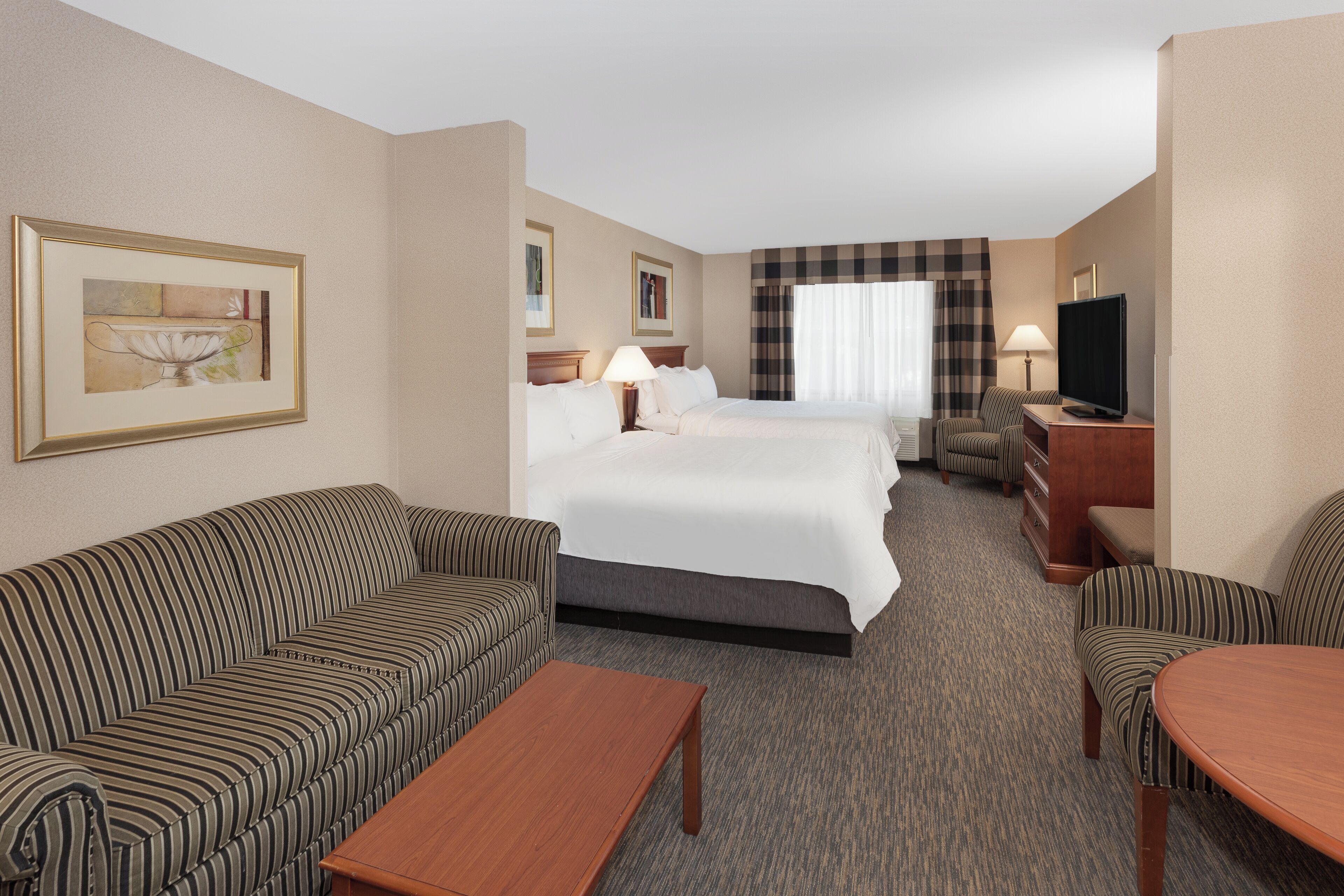 A hotel room with a bed, two sofas, a coffee table, a TV, and a painting on the wall.