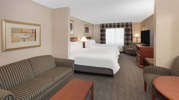 A hotel room with a bed, two sofas, a coffee table, a TV, and a painting on the wall.