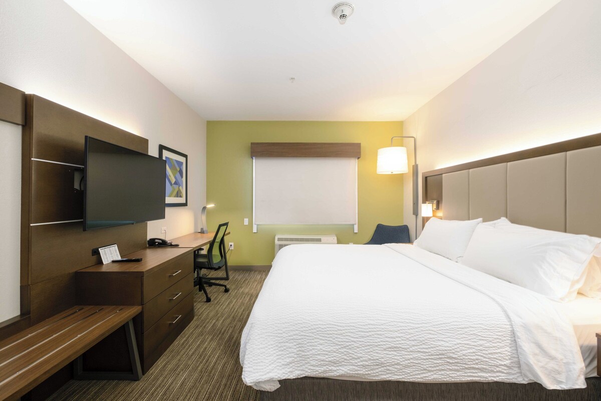 A hotel room with a bed, a desk, a chair, a television, and a wall-mounted air conditioner.