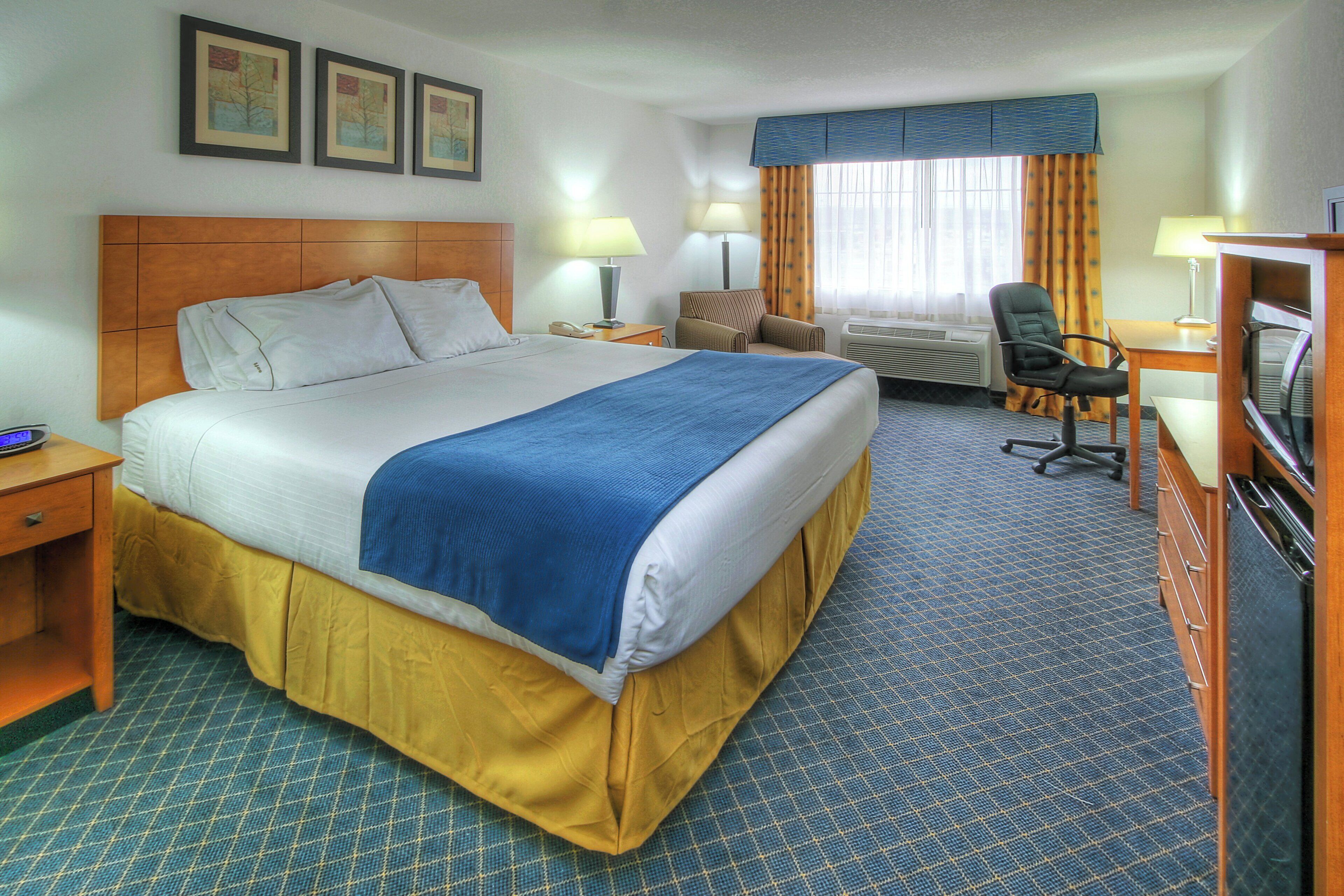 A hotel room with a large bed, a desk with a chair, a television, and a window with curtains.