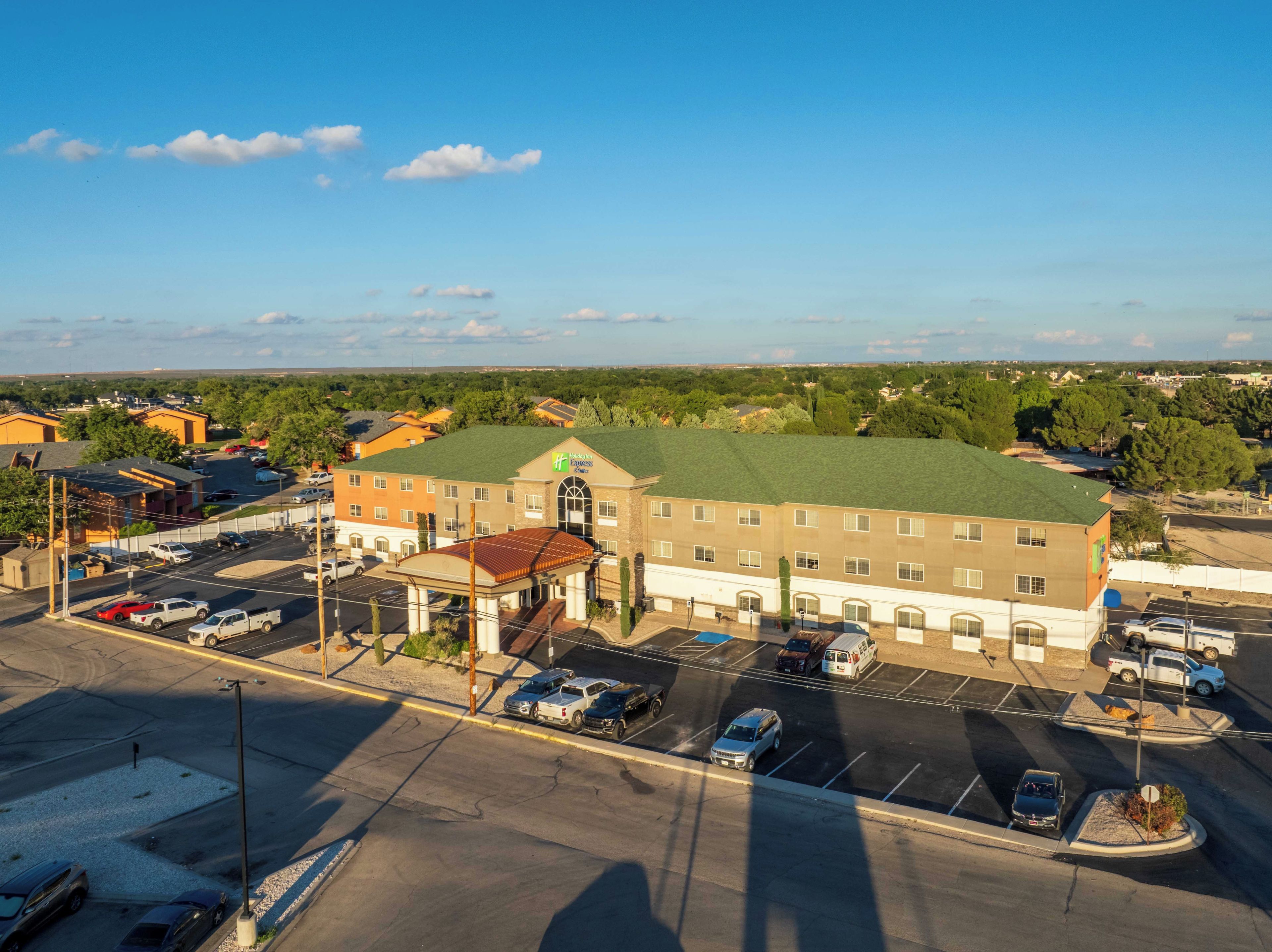 A hotel with a green roof, a parking lot, and a view of the surrounding area.