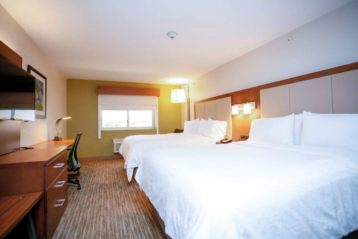 A hotel room with two beds, a desk with drawers, a chair, a lamp, and a window with blinds.