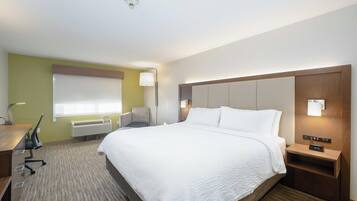 A hotel room with a large bed, a desk with a chair, a lamp, and a nightstand with a clock.