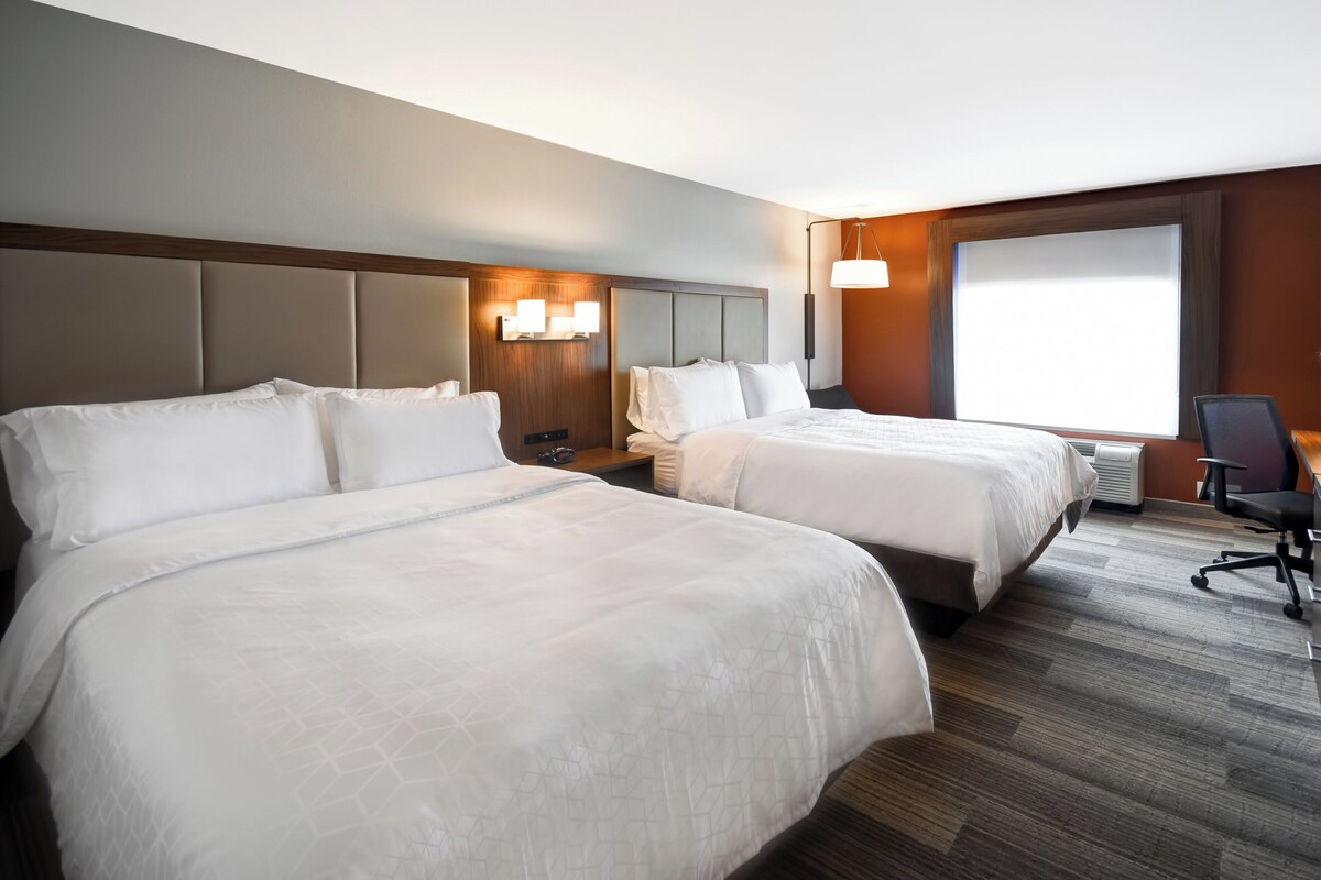 A hotel room with two beds, a desk, a chair, and a large window.
