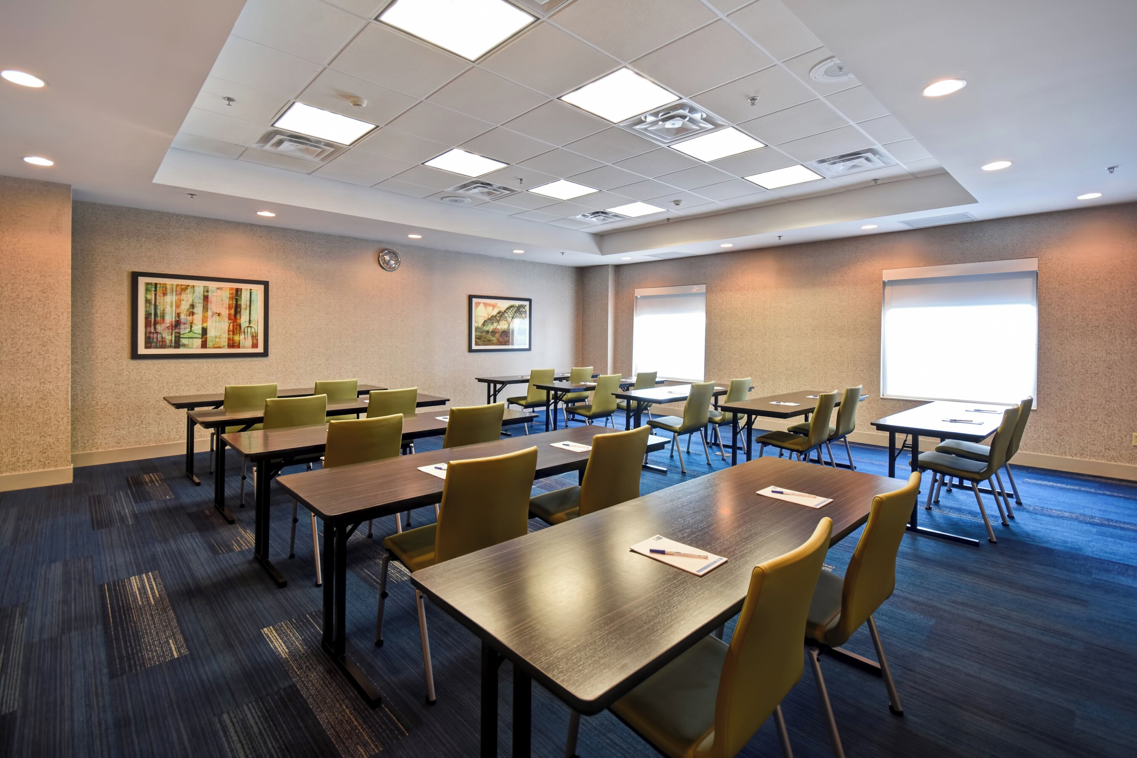 A conference room with multiple tables and chairs, a projector screen, and artwork on the walls.