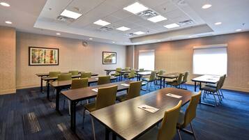 A conference room with multiple tables and chairs, a projector screen, and artwork on the walls.