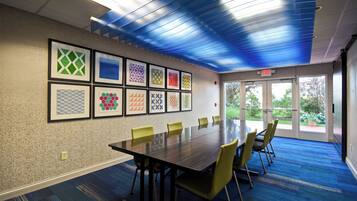 A conference room with a long table, yellow chairs, and framed artwork on the wall.