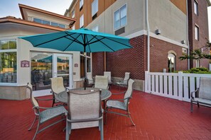 An outdoor seating area with a table and chairs, a blue umbrella, and a brick building in the background. - Holiday Inn Express & Suites Schererville by IHG (Schererville)