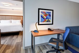 Habitación de hotel con cama, escritorio, silla y un cuadro abstracto enmarco.