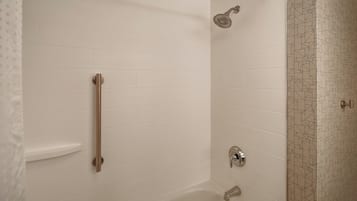 A bathroom with white tiled walls, a shower with a handheld showerhead, a grab bar, and a patterned tile accent wall.