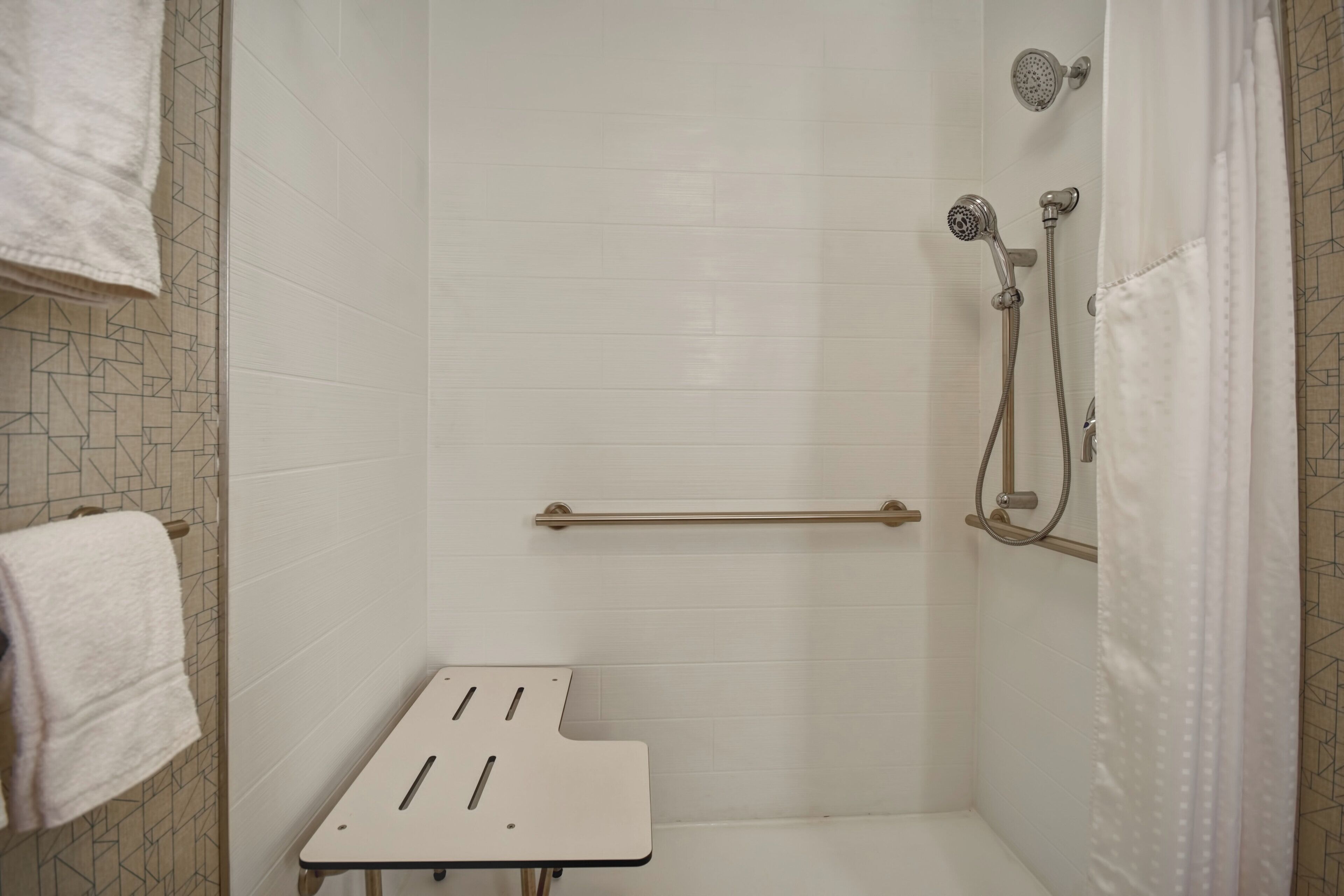 A shower area with a white tiled wall, a handheld showerhead, a towel rack, and a grab bar.