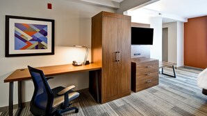 A modern hotel room with a wooden desk, a chair, a wardrobe, a flat-screen TV, and a framed abstract painting. - Holiday Inn Express & Suites Schererville by IHG (Schererville)