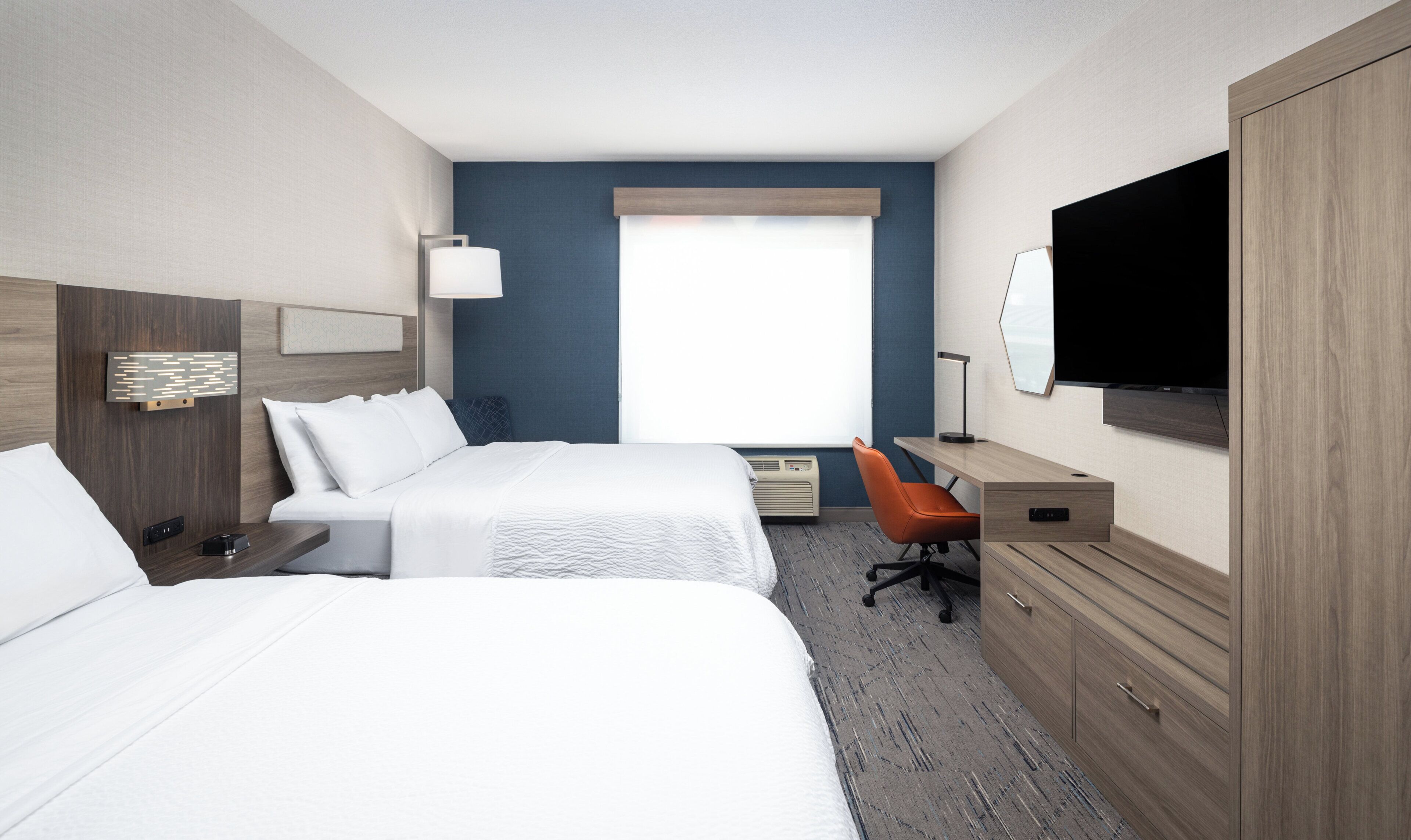 A hotel room with two beds, a desk, a chair, a TV, and a window with blinds.