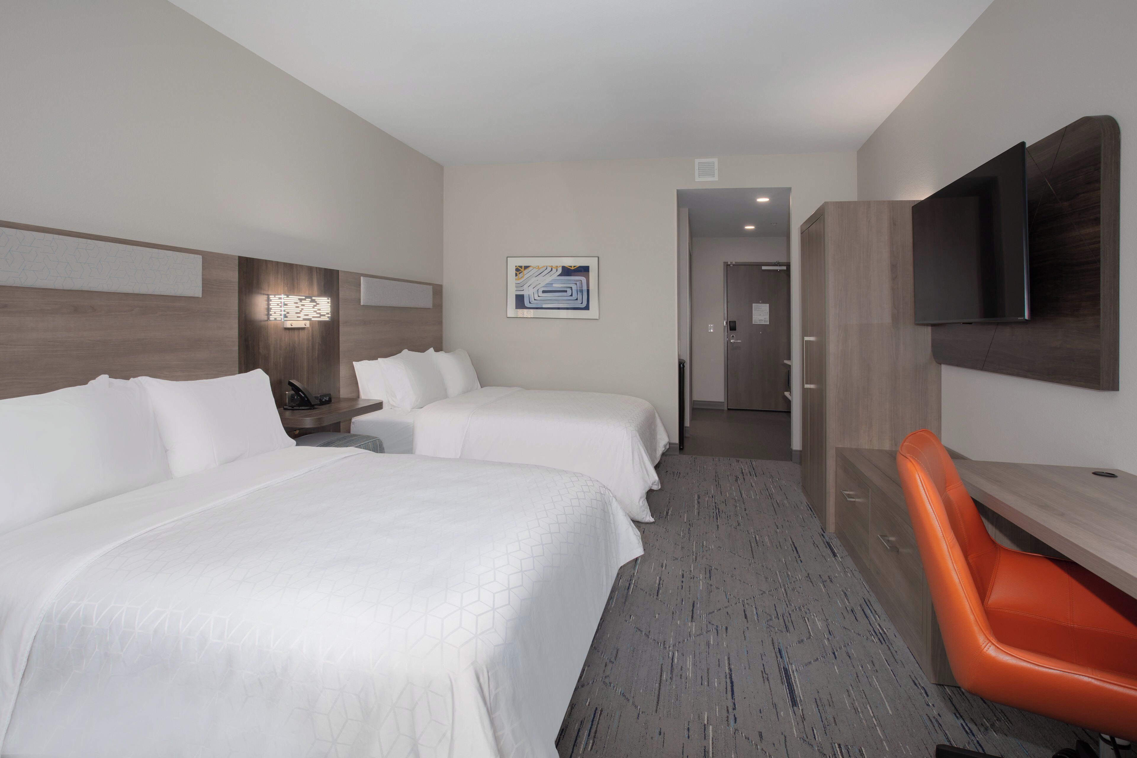 A hotel room with two beds, a desk, a TV, and a bathroom visible in the background.