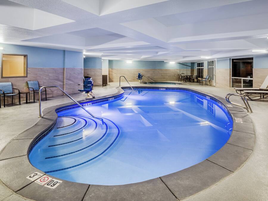 A modern indoor swimming pool with a curved design, seating areas, and a lounge with chairs.
