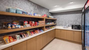 Zona de cuina amb armaris de fusta, microones i prestatges plens de diferents snacks i aliments.