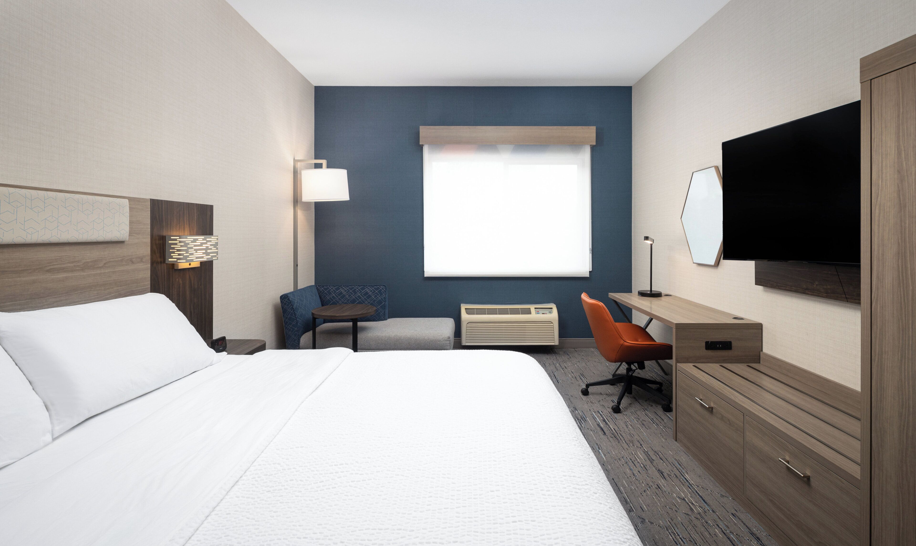 A hotel room with a bed, a desk, a chair, a TV, and a window with blinds.