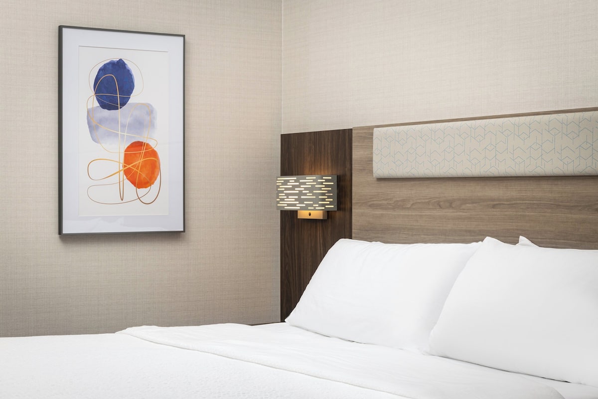 Una camera d'albergo con un letto rifatto con cura, un quadro astratto incorniciato sulla parete e un poggiatesta con motivo geometrico.