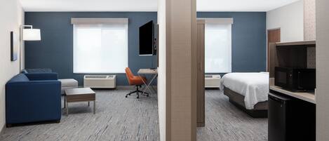 Una habitación de hotel con cama, escritorio, sillón, sofá, televisor y microondas.