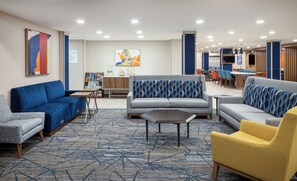 A hotel lobby with a grey sofa, a blue sofa, a yellow armchair, and a coffee table. There is a reception desk with a computer and a magazine rack. - Holiday Inn Express & Suites Nampa - Idaho Center by IHG (Nampa)