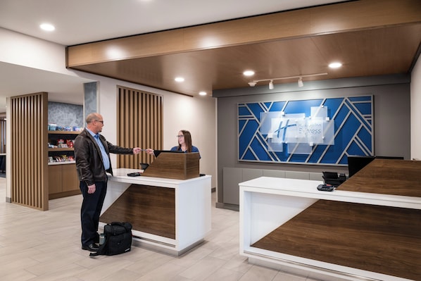 Uma área de recepção de hotel moderna, com balcões de madeira, uma tela digital exibindo informações do hotel e um interior bem iluminado.