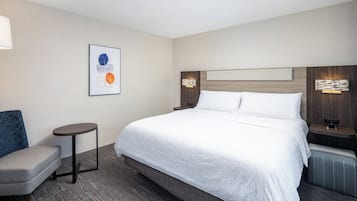 Una habitación de hotel con una cama grande, una mesa redonda pequeña, una silla y una obra de arte colgada en la pared.