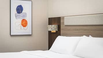 Une chambre d’hôtel avec un lit parfaitement fait, une œuvre d’art abstraite encadrée au mur et une tête de lit ornée d’un motif géométrique.