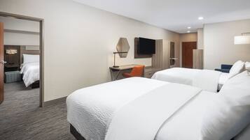 Habitación de hotel con dos camas, un escritorio, una silla, un televisor y una puerta que da a otra habitación.