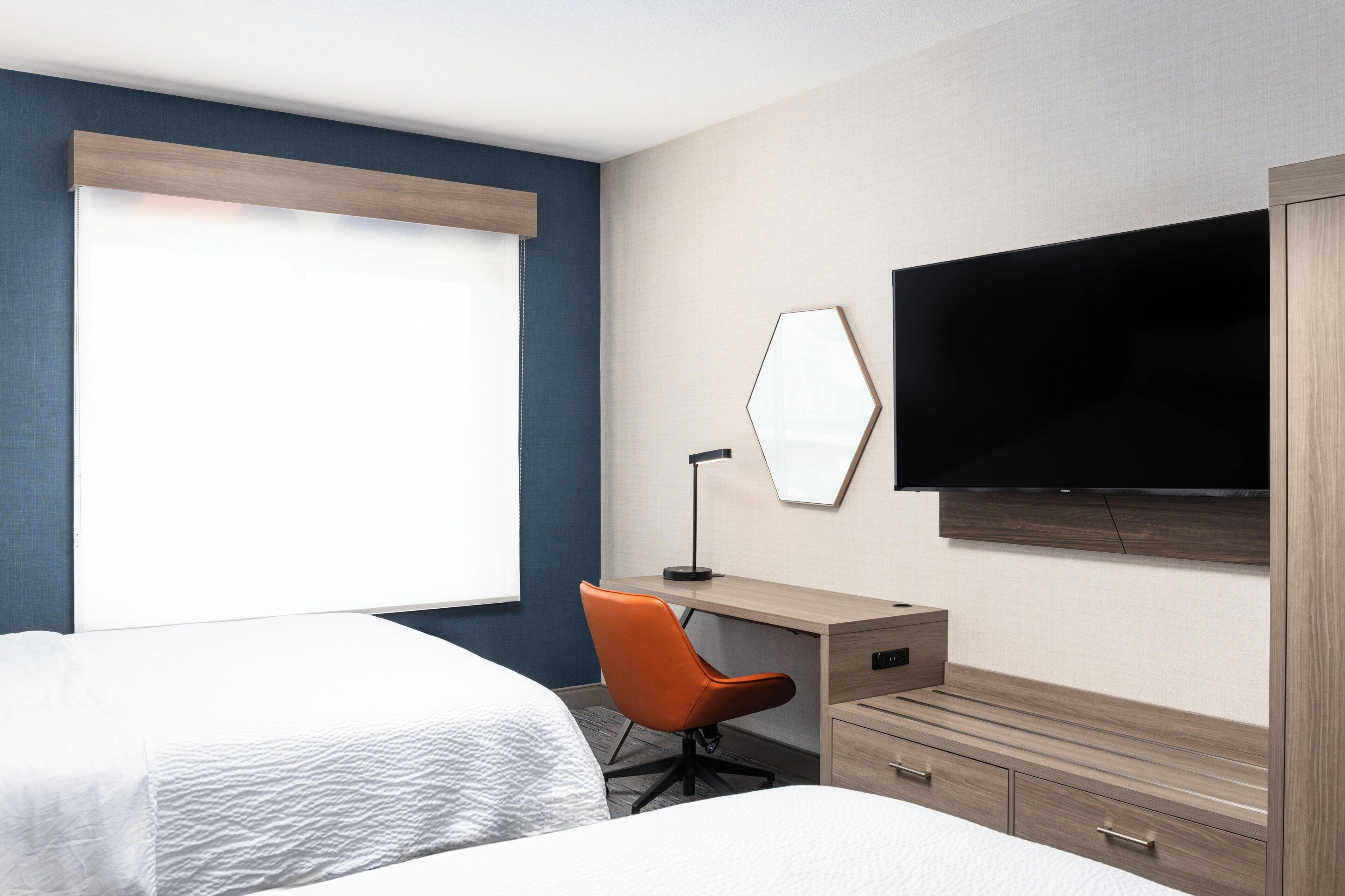 A hotel room with two beds, a desk, a chair, a television, and a wardrobe.