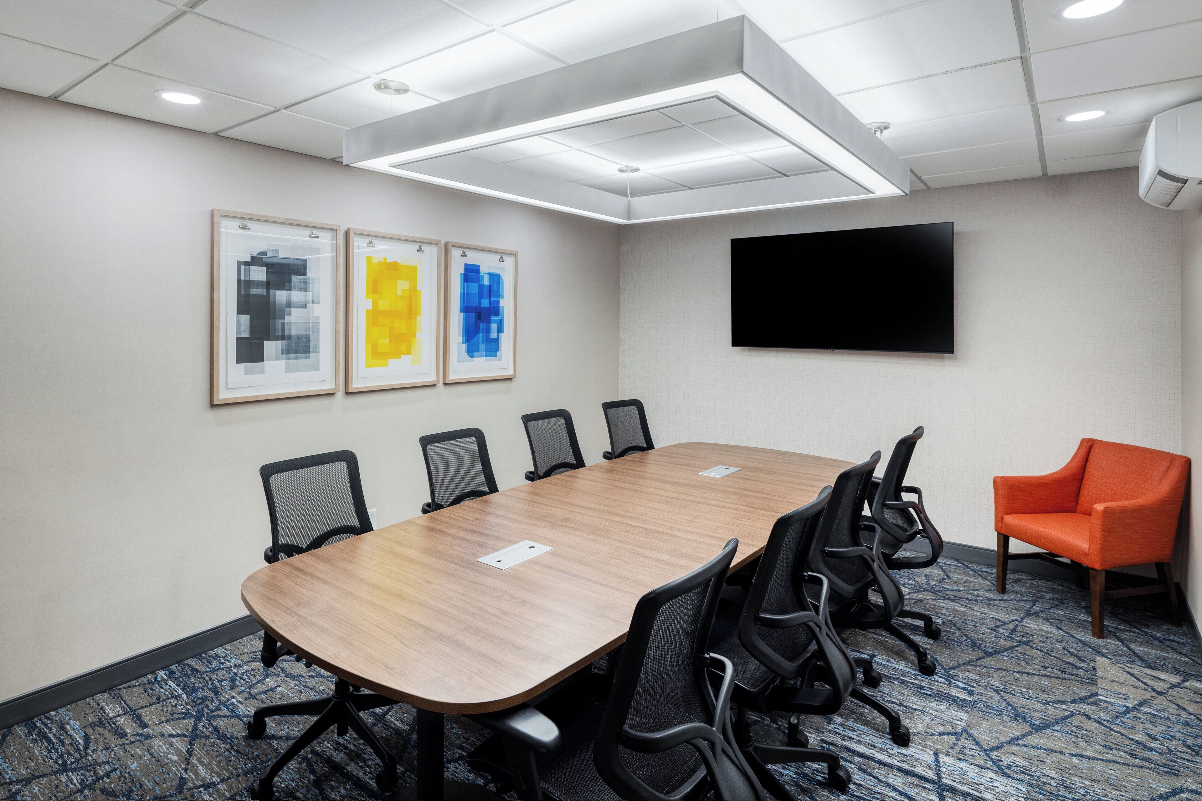 A conference room with a long table, six chairs, a TV, and artwork on the wall.