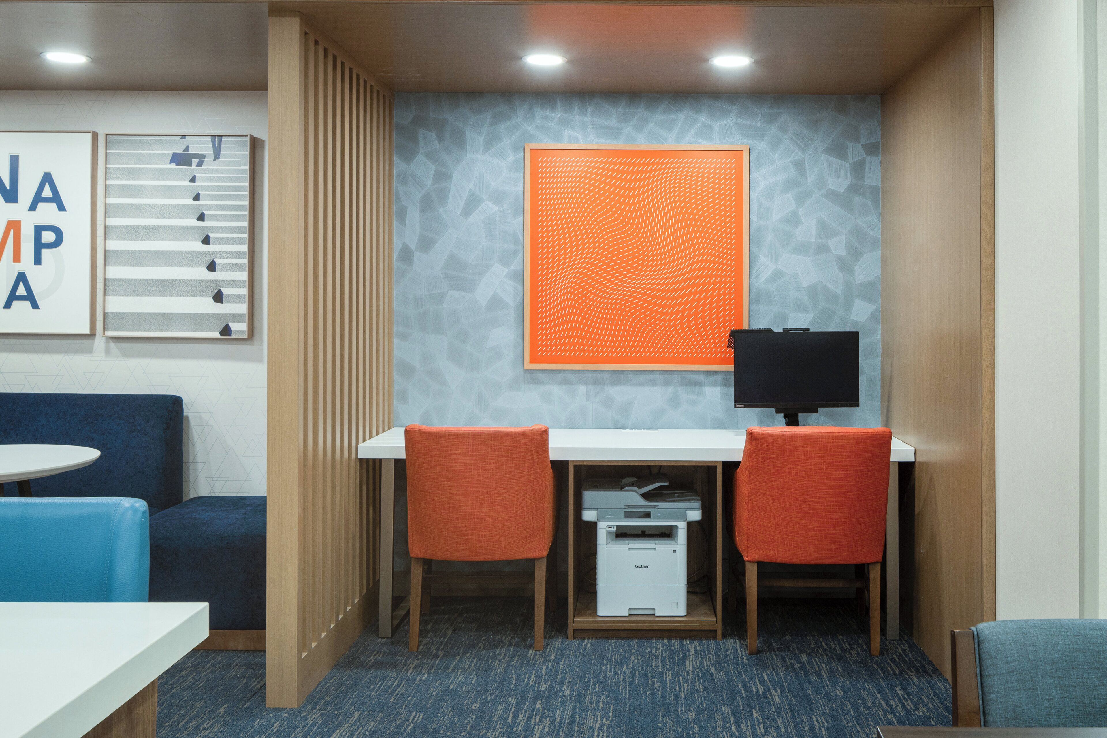 A modern office space with a white desk, two orange chairs, a printer, and a large orange textured wall.