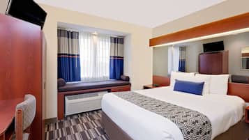 A hotel room with a bed, a desk, a chair, a window with curtains, a television, and a mirror.