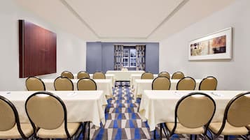 Un salón de conferencias con suelo a cuadros, mesas blancas y sillas color beige.