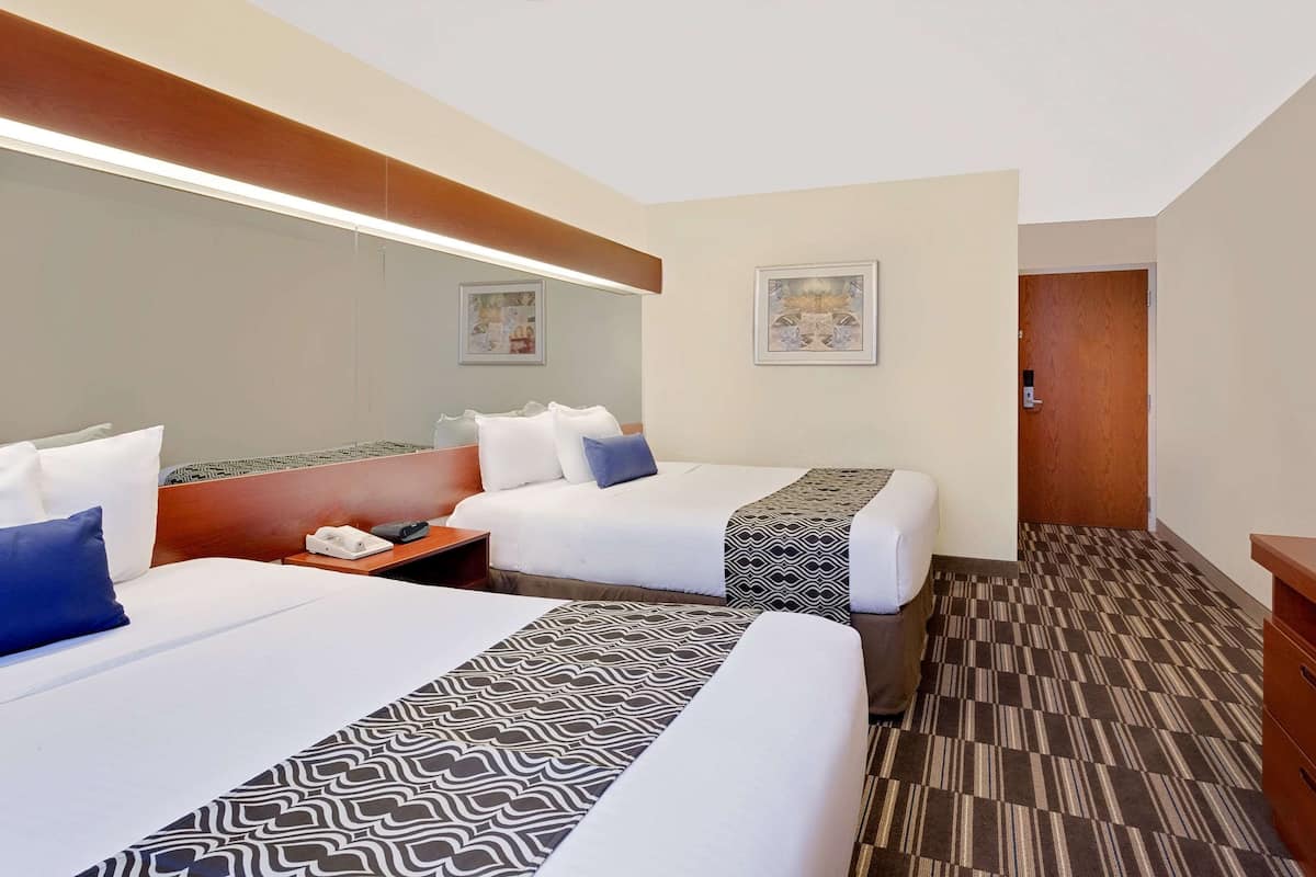A hotel room with two beds, a wooden headboard, a bedside table with a phone, and a patterned bed runner.
