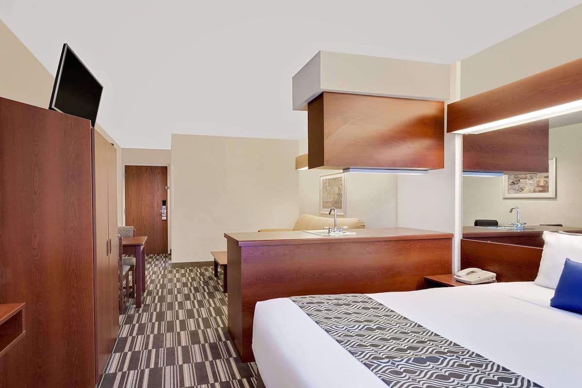 A hotel room with a bed, a desk, a chair, a wardrobe, and a bathroom mirror.