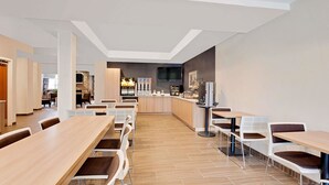 A modern dining area with long tables and chairs, a bar area with a TV, and a kitchen in the background. - Microtel Inn & Suites by Wyndham Middletown (Middletown)