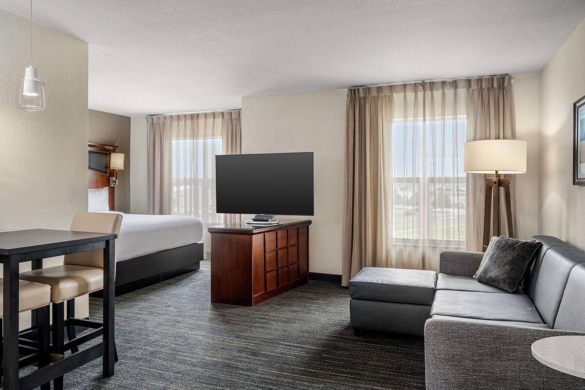 Una habitación de hotel con cama, televisor, escritorio, sofá y lámpara.
