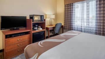 Ein Hotelzimmer mit Bett, Fernseher, Schreibtisch mit Computer, Mikrowelle und Kaffeemaschine.